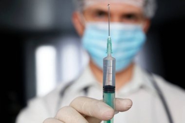 Doktor elinde şırınga, tıbbi maskeli adam ve enjeksiyona hazırlanan koruyucu eldivenler. Covid-19 salgını sırasında aşı kavramı