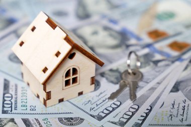 Ahşap ev modeli ve arka plandaki Amerikan doları banknotları. Konut piyasası, emlak satın alma veya kiralama