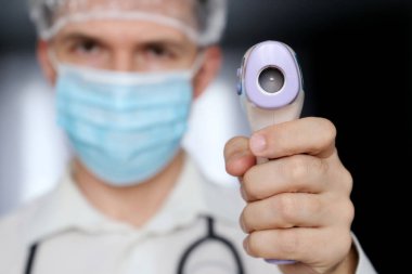 Tıbbi maskeli adam vücut ısısını, koronavirüsü belirtilerini ölçer. Elinde dijital izometrik temas olmayan termometresi olan doktor, covid-19 karantinası sırasında güvenlik önlemleri