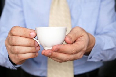 Ofis elbiseli ve kahveli bir adam. Erkeklerin elinde beyaz bir bardak sıcak içecek, ofiste çalışırken mola.