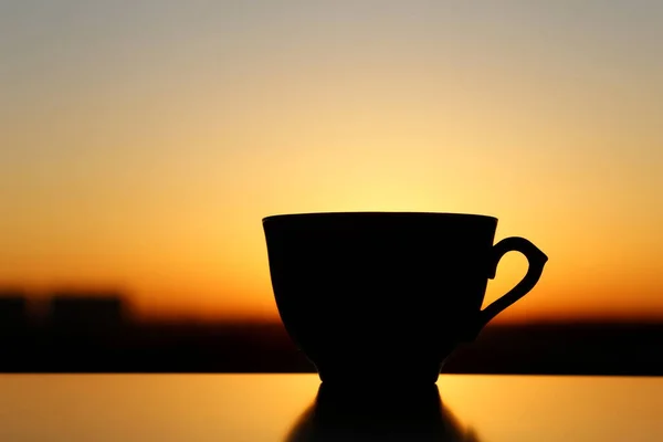 Silhouette of coffee cup on sunrise background, fresh start in the morning. Cozy atmosphere, city view from the window