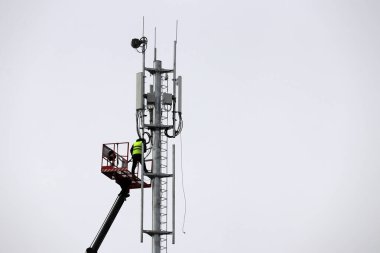 İşçi kaldırma platformunda duran baz istasyonunu onarıyor. Gökyüzü arka planında mobil telekomünikasyon donanımı