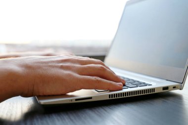 Günbatımında pencerenin yanındaki dizüstü bilgisayarın başında oturan adam, erkek eli kapanıyor. Konforlu iş yeri, çevrimiçi iletişim, ofis ya da ev işi kavramı