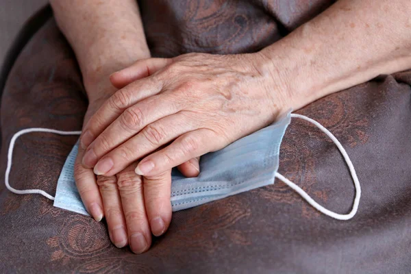 Wrinkled hands of elderly woman with medical face mask. Coronavirus protection for old people