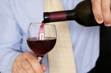 İş elbiseli bir adam şişeden kırmızı şarap dolduruyor. Ofiste şirket partisi, restoranda romantik yemek ya da diplomatik kabul konsepti.