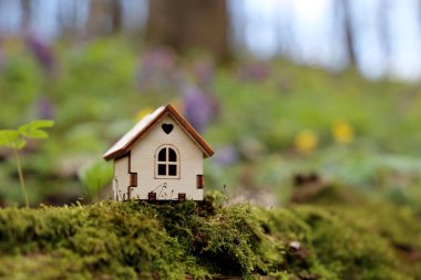 Bahar çiçeklerinin arka planında bir ormanda ahşap ev modeli. Kır evi kavramı, ekolojik olarak temiz bir alanda gayrimenkul, peri doğasının canlı renkleri