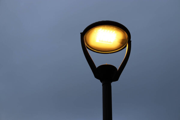 Светящаяся лампа на фоне вечернего неба. Электрическое освещение, энергосберегающие уличные фонари