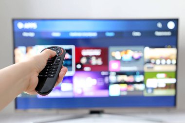 Akıllı ekran arka planında uzaktan kumandalı bir kadın el. Ses kontrolü, yayın hizmetlerini seçen, film izleyen kişi.