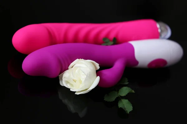 Adult toys and white rose on a dark glass background, romantic gift for sex. Purple silicone vibrator, pink dildo and fresh flower