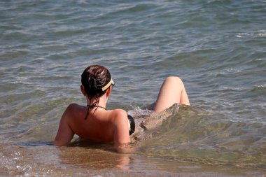 Woman in swimsuit relaxing in sea water lying on a sand. Beach vacation, summer leisure