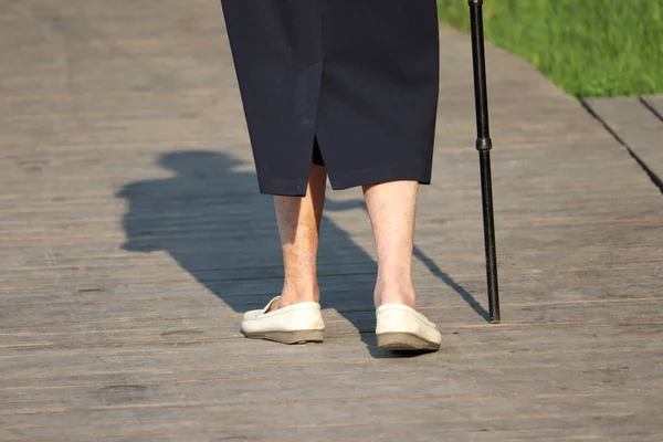 通りを杖で歩くお年寄りの女性 夏の公園の木製の歩道上の女性の足 障害の概念 人を制限します 背骨の病気 高齢者 — ストック写真