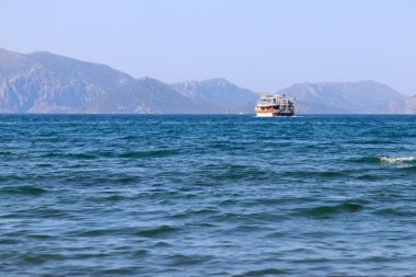 Sisli arka planda Ege Denizi 'nde yelken açan turistlerle dolu tekneye odaklı olmayan manzara. Yaz tatili ve seyahat