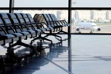 Empty waiting chairs in the airport building against the plane on runway. Travel during quarantine at coronavirus pandemic