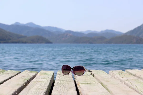 Zonnebril Een Oude Houten Pier Zee Mistige Bergen Achtergrond Zomervakantie — Stockfoto