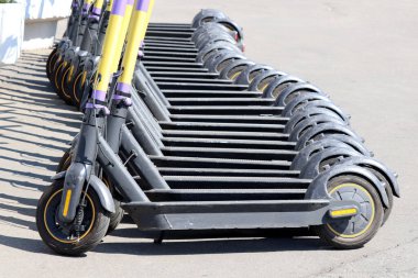 Otoparkta arka arkaya elektrikli scooterlar. Şehir bisiklet kiralama sistemi, sokakta elektronik scooterlar.