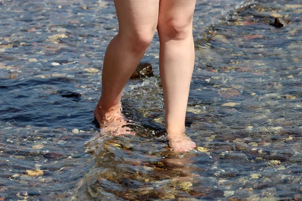 裸足の女性は海の波の中で小石の上を歩く サーフウォーター ビーチバケーションで裸の女性の足 — ストック写真