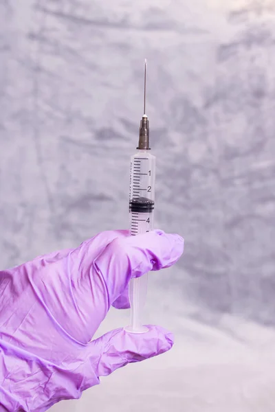 A gloved hand holds a syringe on gray background