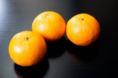 Siyah ahşap bir masada üç sarı mandalina. Yaklaş.