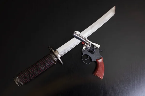Samurai sword and pistol on wooden table close up