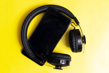 Sarı arka planda kulaklık ve telefon yakın plan.