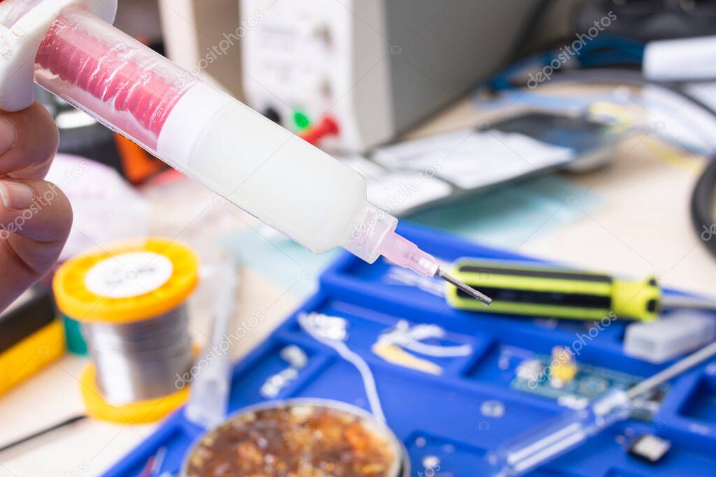 Syringe with flux on engineer's desktop background close up