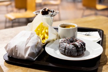 Donut, bir fincan kahve ve patates kızartması tepside yakın çekim.