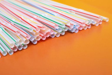 Turuncu arka planda içmek için bir yığın plastik pipet.