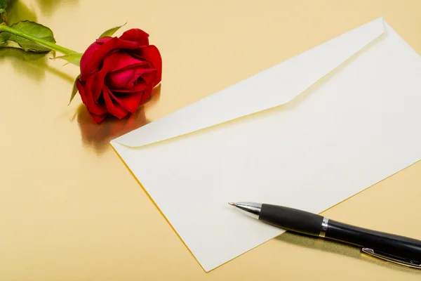 Beautiful red rose an envelope and a pen on a gold background — Stock Photo, Image