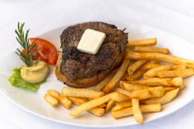 ızgara etler ve beyaz bir tabak kızarmış patates