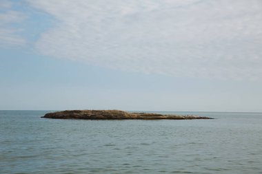 Hazar Denizi bulutları ve küçük bir ada. Deniz kenarındaki mavi gökyüzü.