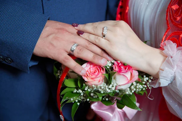 They put their hands on the red and white rose . Bride and groom with Engagement gold rings put their hands . The girl and the boy put their hands . The girl and the boy put their hands on white roses