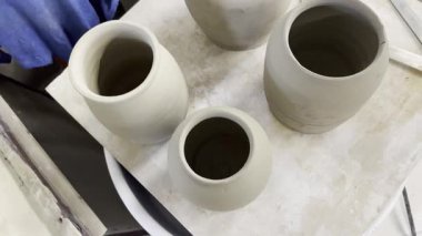 Seramik kil ürünleri raf yakın çekim üzerinde durmak. Heykeltraş beyaz kil tencere urun sculpts. Karanlık. Atölye seramik. Ana sakat. Kültürel gelenekleri. El yapımı. Zanaat. Bükülmüş potters tekerlek.