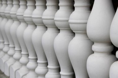 Düz bir çizgide dizilmiş bir dizi beyaz baluster. Her baluster basit bir tasarım gösteriyor. Ayarlar parlak ve net, mimarinin detaylarını ortaya koyuyor..
