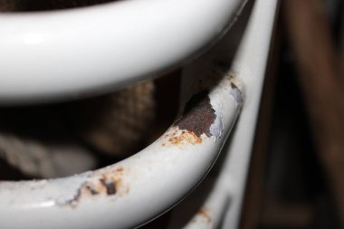 Beyaz metal bir nesne gölgeli bir bölgede yüzeyinde pas olduğunu gösteriyor. Nesnede çizikler ve soyulmuş boyalar var. Zaman içinde sık sık kullanıldığı için yaşlanma durumunu gösteriyor..