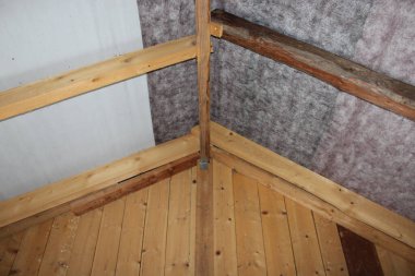 Odanın köşesinden ahşap kirişler ve duvarlar görünüyor. Odak noktası, ahşaptan yapılmış kırsal bir ortamda tavan yapısı..