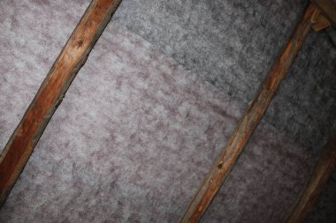 Tahta kirişler izolasyon malzemesi olan bir tavanda görülebilir. İnşaat alanı parlak ve devam eden bir çalışmayı gösteriyor. Malzemelerin ayrıntıları açık..