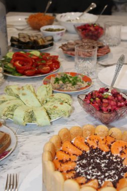 Bir grup insan salata, et ve tatlı da dahil olmak üzere farklı yemeklerle dolu bir masada yemek yemekten zevk alıyor. Dekor renkli yiyeceklerle dolu neşeli bir atmosfer gösteriyor..