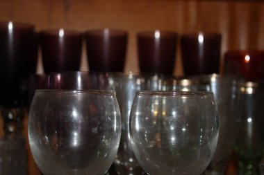 Temiz bardaklar, siyah mumların önündeki rafta durur. Mumların sıcaklığı gece boyunca odada yumuşak bir ışık yaratıyor..