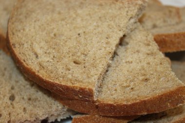 Tam tahıllı ekmek dilimleri bir masanın üzerine istiflenir. Bir dilim ikiye bölünmüş, iç dokuyu ve rengi gösteriyor. Ayarlar basit ve ekmeğe odaklı..