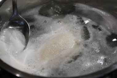 Bir insan hamurun piştiği yerde bir kaşık dolusu kaynar suda kaşık karıştırır. Sahne buharın yükseldiğini ve suyun içinde kabarcıklar oluştuğunu gösteriyor..