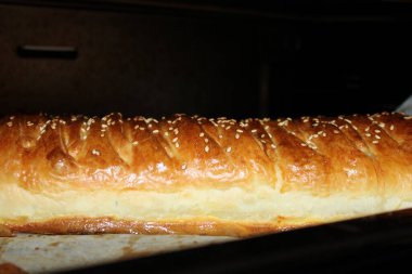 Sabah, susam tohumlu uzun bir somun ekmek bir fırında pişiyor. Hamur pişerken altın hamuru görülebilir. Kokusu mutfağı dolduruyor..