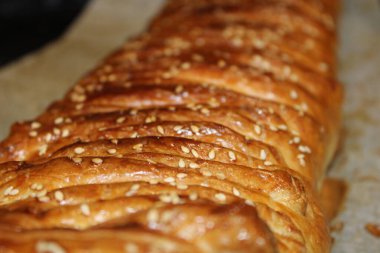 Hamur işi altın kabuklu ve susam tohumuyla kaplıdır. Mutfaktaki bir çarşafa konur. Sahne uzaya gelen sıcak ışığı gösteriyor..