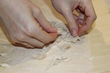 Mutfağın ahşap yüzeyinde iki el ince et şeritlerini yırtıyor. Hazırlıklar akşam yapılacak. Malzemelerin dikkatli bir şekilde kullanılması gösterilecek..