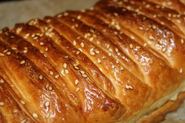 Pişmiş uzun bir parça hamur, altın kabuğunu ve serpiştirilmiş susam tohumlarını gösteren bir tepsinin üzerinde duruyor. Mutfak aydınlık görünüyor, servis için hazır..