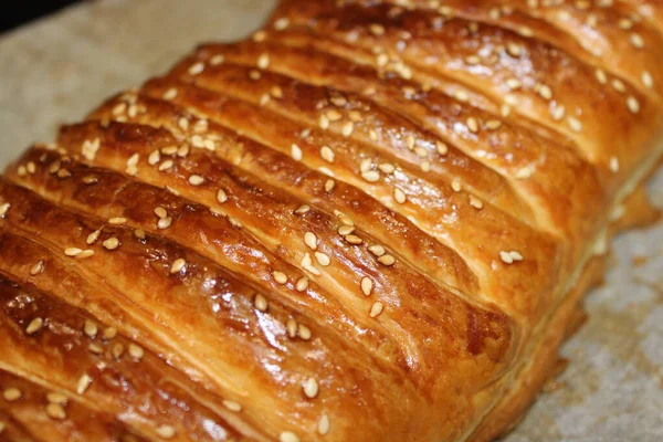 Sıcak bir hamur işi servis edilmeye hazır. Kabuğu parlak ve kahverengi, üzerine susam tohumları serpiştirilmiş. Mutfakta ayrıntıları vurgulayan güzel bir ışıklandırma var..