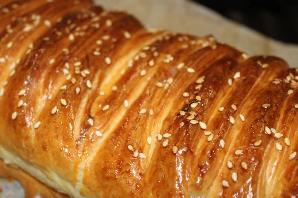 Fırın tepsisinde altın kahverengi kabuklu uzun bir hamur işi yatıyor. Üzerinde susam tohumları var ve sıcak, mutfaktan servis edilmeye hazır..