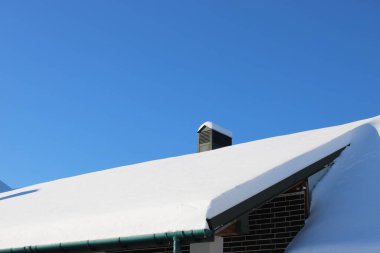 Kar evin çatısında yoğundur. Bir baca dimdik ve gökyüzü bulutsuz mavidir. Sahne, sakin bir mahallede kış havasını gösteriyor..