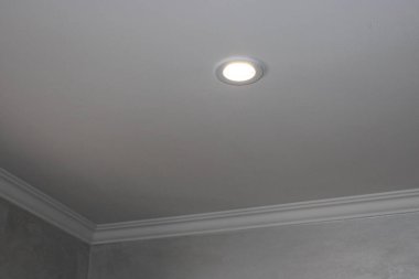 Bir odadaki sade bir tavana lamba yerleştirilir. Mekan, nötr renklerle ve pürüzsüz yüzeylerle modern tasarım tarzını gösteren minimalist bir görünüme sahip..