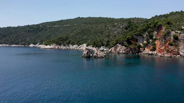 Uitzicht op een drone vanuit de lucht over een rotsachtige kustlijn, kristalhelder zeewater in de Egeïsche Zee, toeristische stranden en veel groen op het eiland Skopelos, Griekenland. Een typisch uitzicht op vele gelijkaardige Griekse eilanden. — Stockfoto