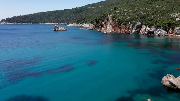 Uitzicht op een drone vanuit de lucht over een rotsachtige kustlijn, kristalhelder zeewater in de Egeïsche Zee, toeristische stranden en veel groen op het eiland Skopelos, Griekenland. Een typisch uitzicht op vele gelijkaardige Griekse eilanden. — Stockfoto